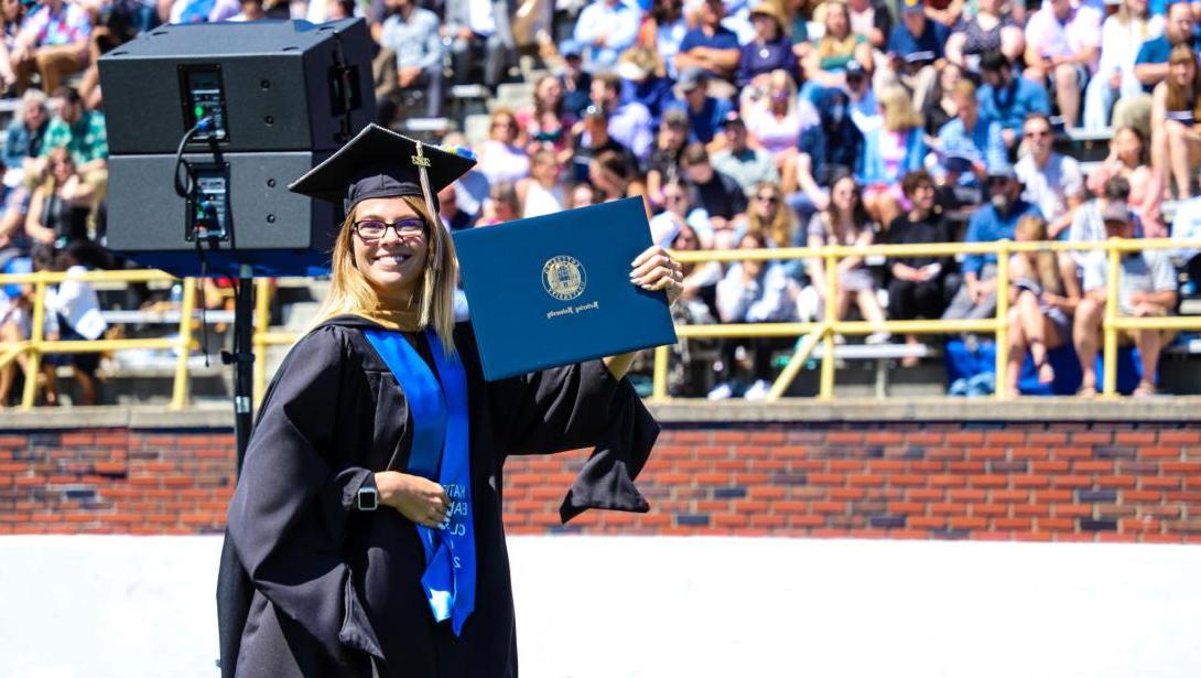 A Kettering University student in cap and gown holding a diploma at graduation